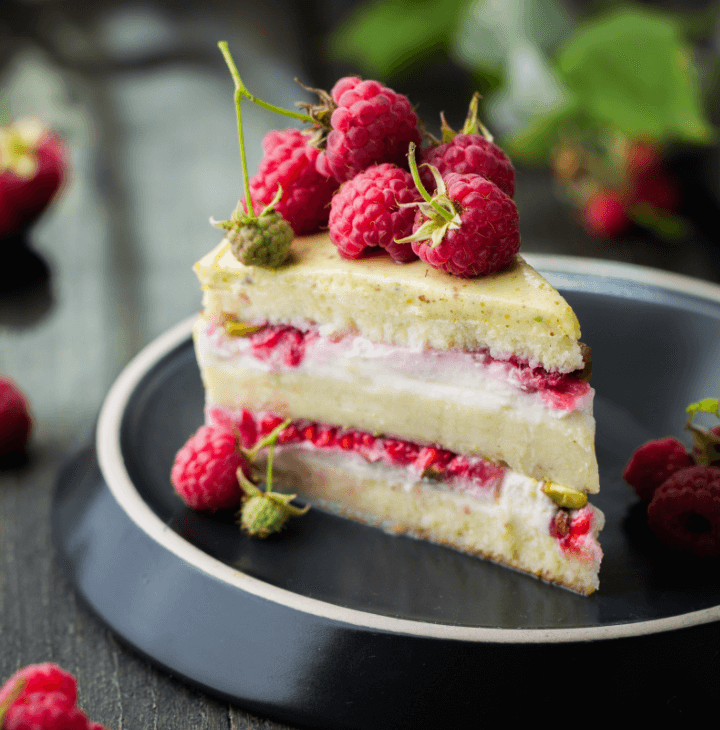 A raspberry layer cake slice with fresh raspberries on top. Served on a fancy plate.